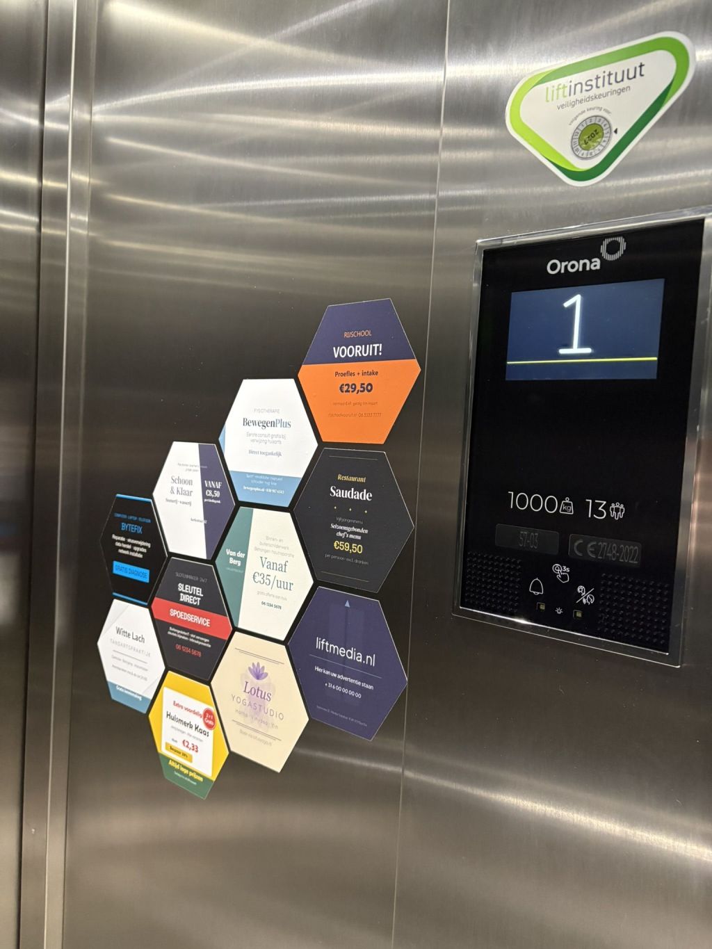 A real LiftMedia installation: hexagon sticker ads from local businesses on the wall of an Amsterdam elevator, next to the floor display